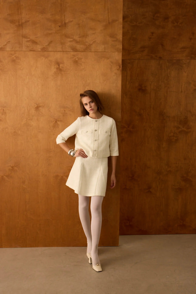 Woman in a white outfit standing against a brown wall